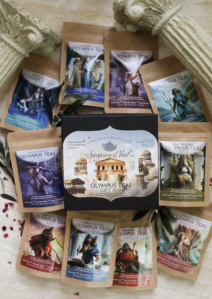 A gift box of Simpson &amp; Wailz Olympus Teas surrounded by multiple individual tea pouches with various mythological and historical illustrations, arranged on a light textured surface with decorative stone pillars.