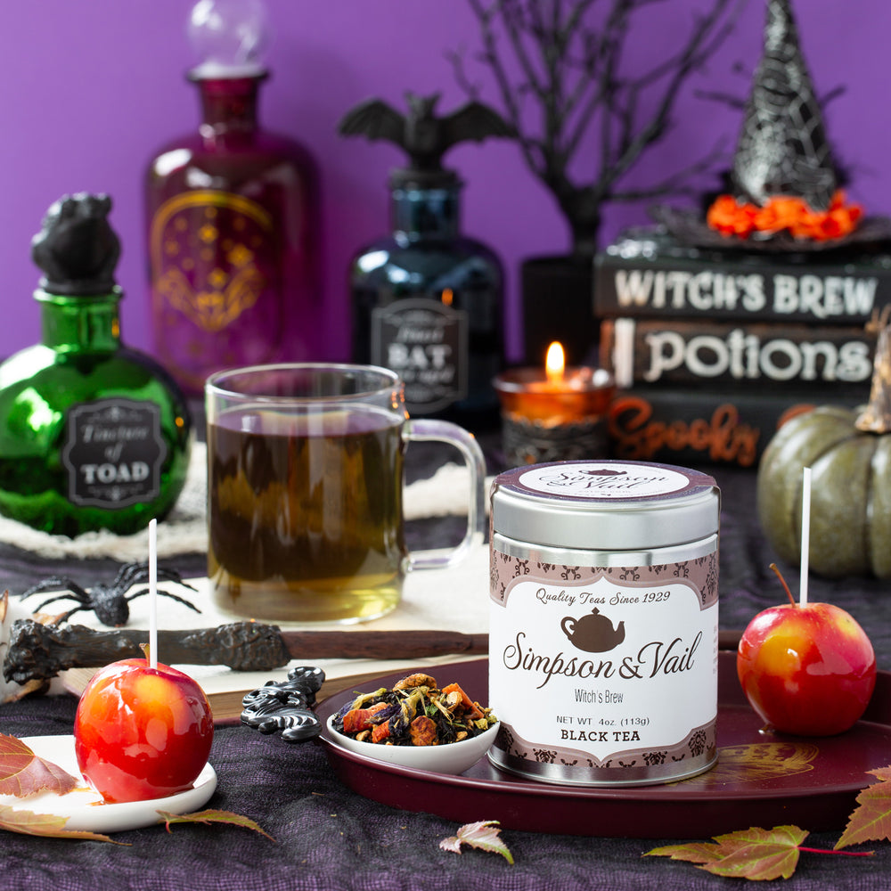 Halloween-themed setup with a mug of tea, candy apples, and a canister labeled 'Simpson & Vail' on a purple background.